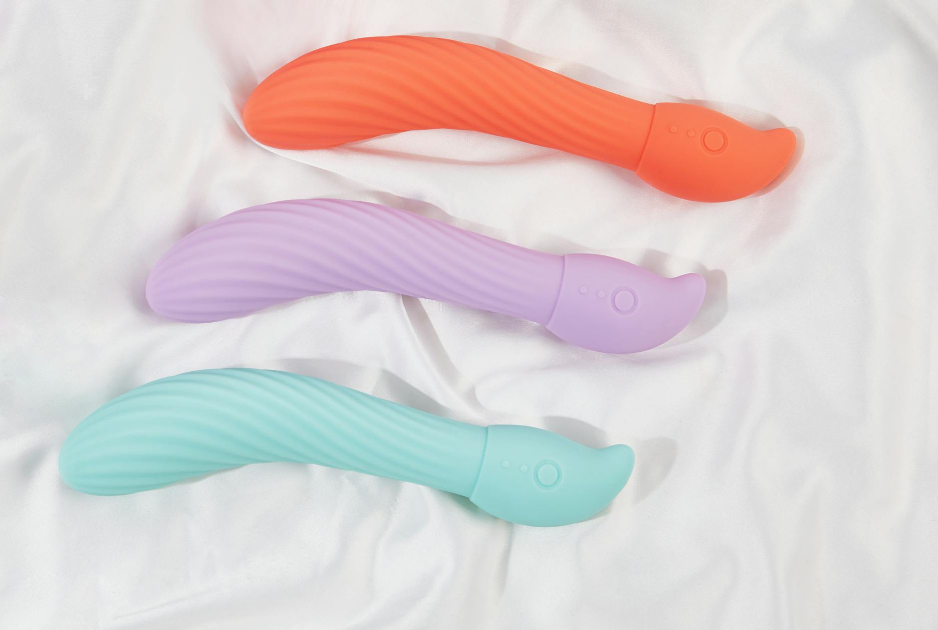 Three colorful vibrators arranged on white fabric, showing smooth texture and design detail