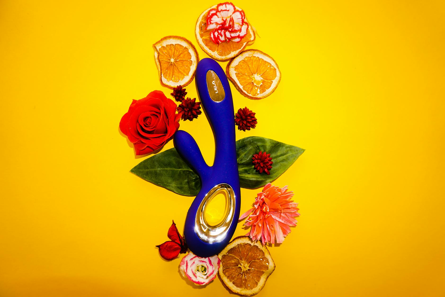 Blue clitoral vibrator surrounded by fresh lemons and flowers on a yellow background